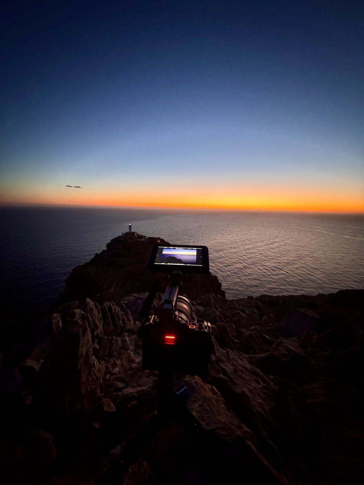 Kamera am Klippenrand zur blauen Stunde, Leuchtturm überm Meer