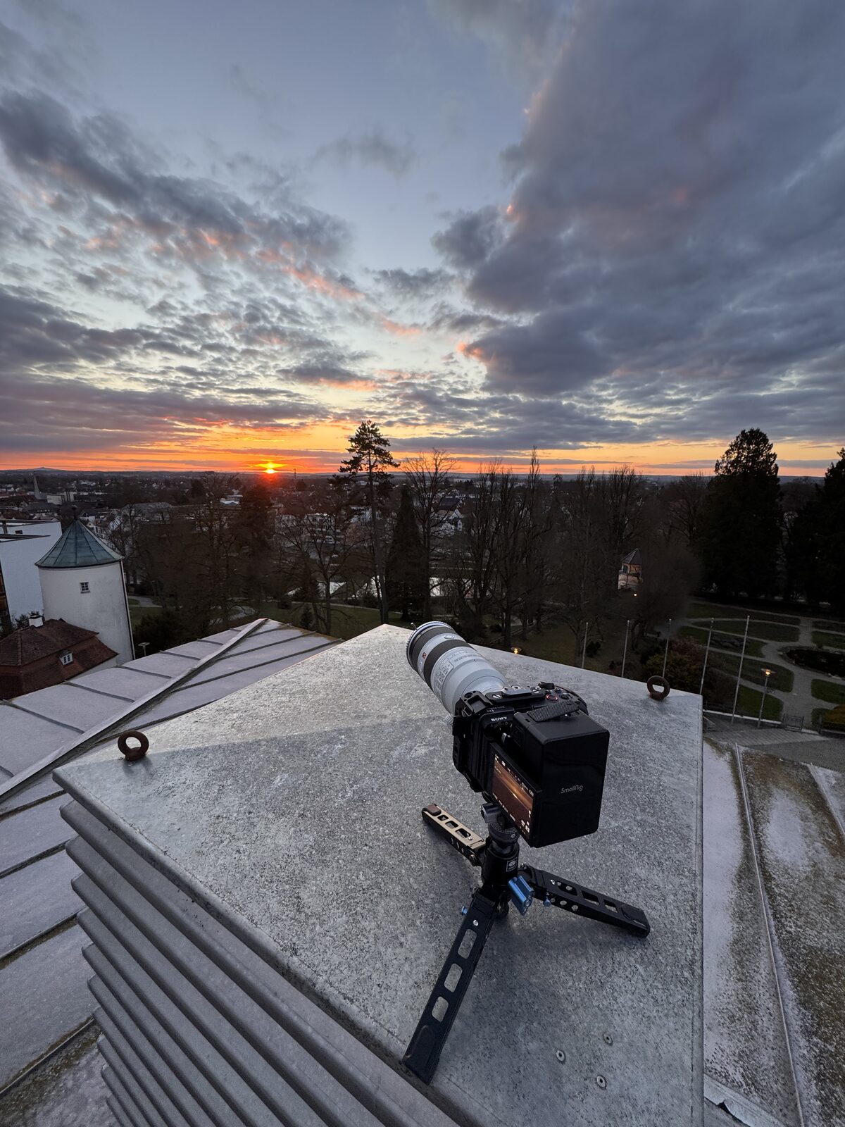 Kamera mit Teleobjektiv auf einem Dach über der Stadt bei Sonnenuntergang